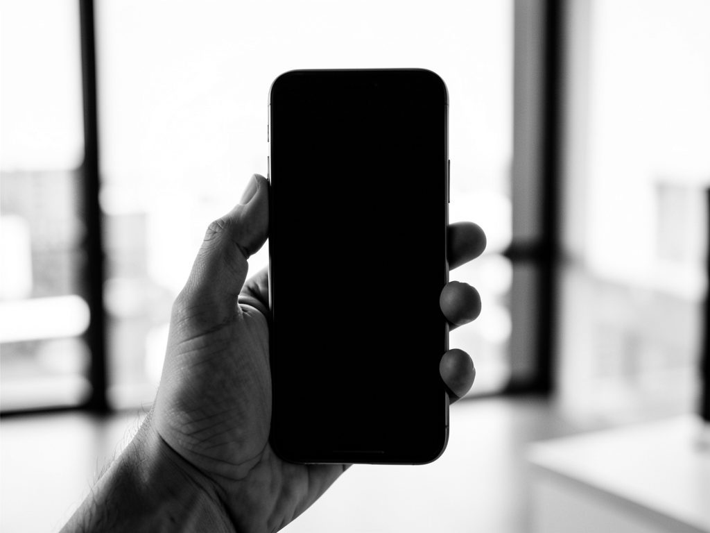 Infotraq Apps: a hand holding a smartphone in front of a window, in black and white